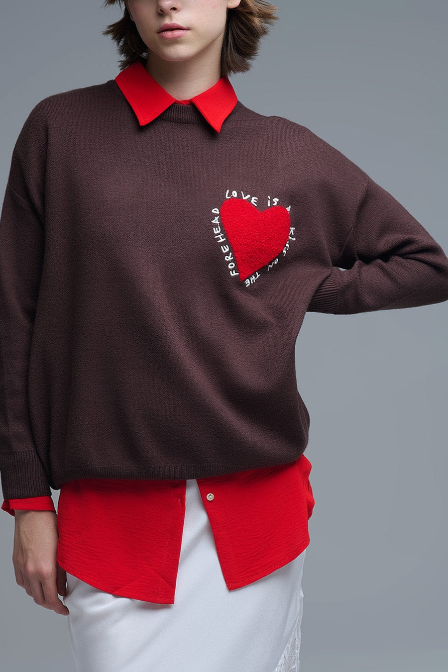 Plano medio de un jersey de punto marrón con un corazón rojo texturizado y el texto 'Love is...' bordado.