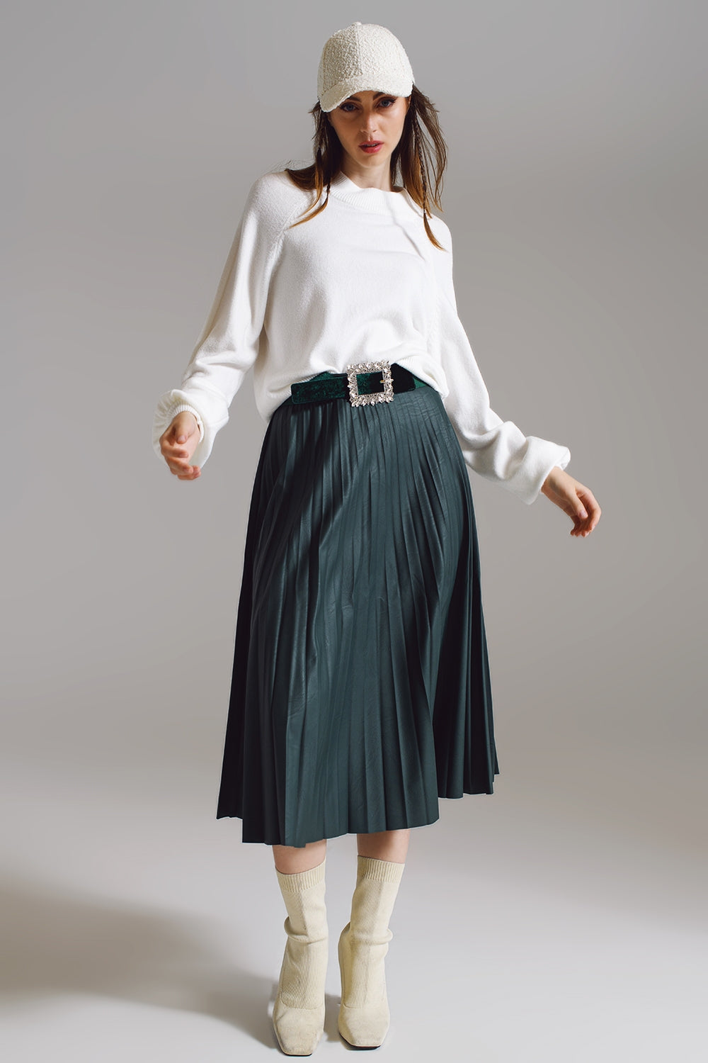 Modelo con look completo de jersey de punto blanco roto con mangas globo y falda midi plisada verde.