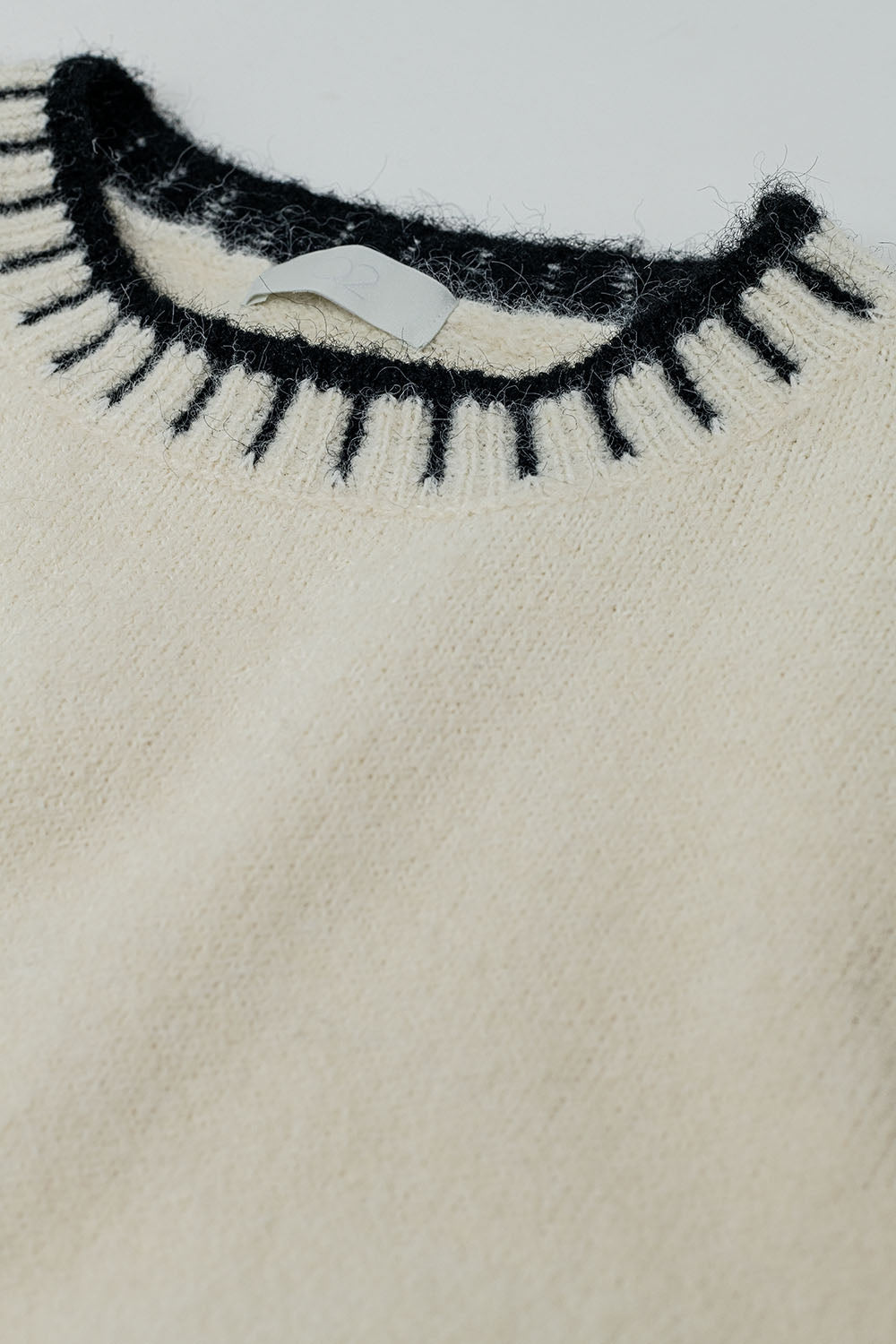 suéter de punto esponjoso color crema con detalles de canalé negro en cuello y puños.