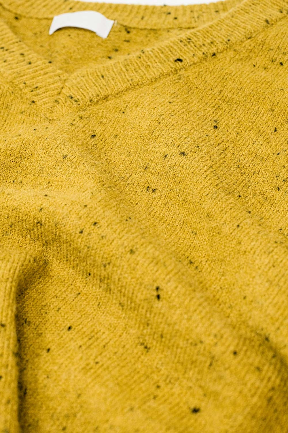 Primer plano de la textura de un tejido de punto moteado en color mostaza.