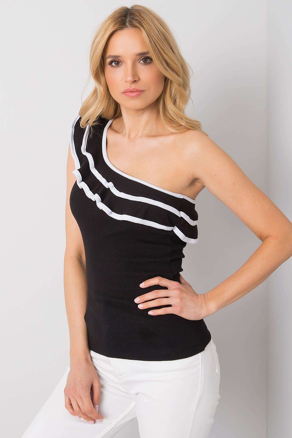 Detalle lateral del top negro con volante y escote al hombro.