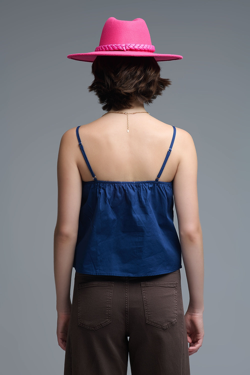 Top azul marino de tirantes con un gran lazo estructurado en el pecho, combinado con pantalones marrones.