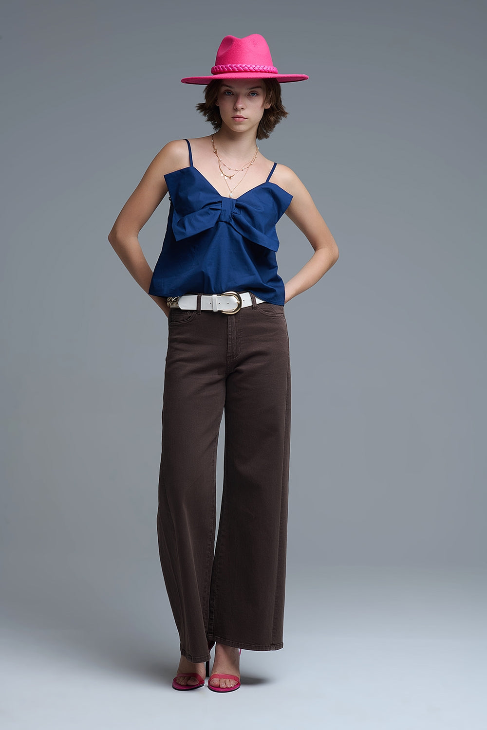 Top azul marino de tirantes con un gran lazo estructurado en el pecho, combinado con pantalones marrones.