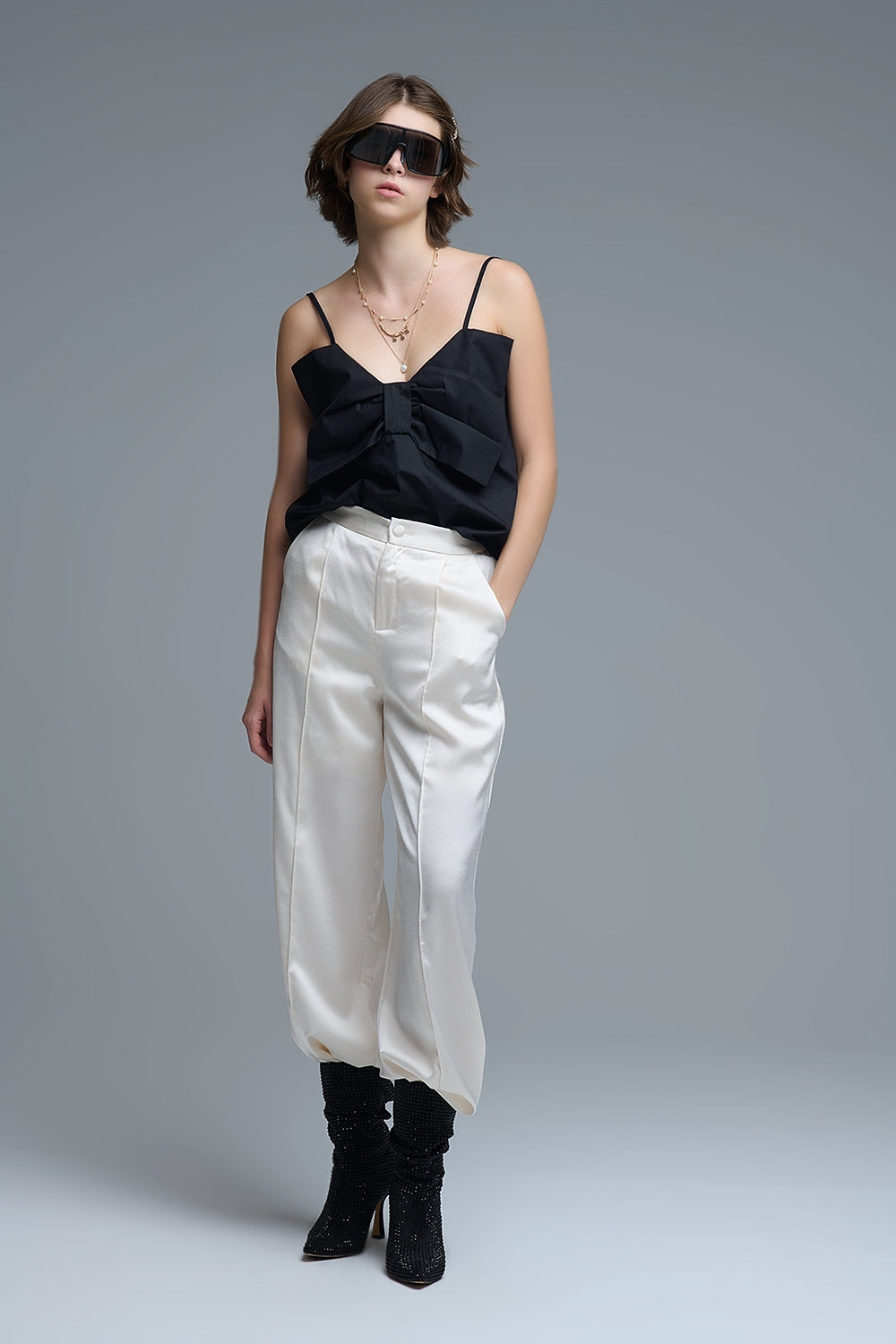 Top negro de tirantes con un gran lazo estructurado en el pecho, combinado con pantalones blancos de vestir.