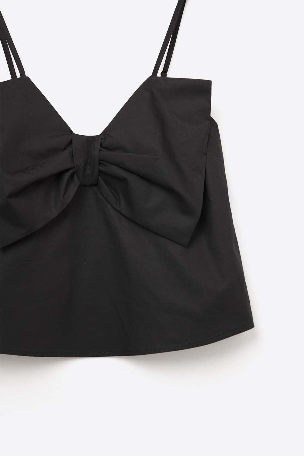 Top negro de tirantes con un gran lazo estructurado en el pecho, combinado con pantalones blancos de vestir.