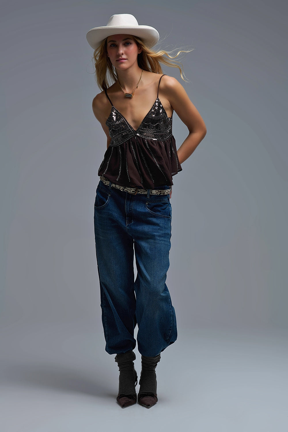 Mujer con sombrero blanco vistiendo un top de tirantes marrón con lentejuelas bordadas y vaqueros.