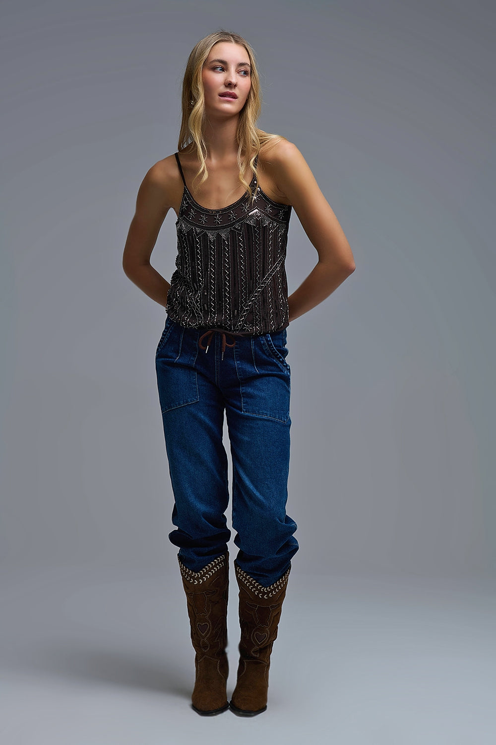 look completo de botas cowboy y vaqueros combinados con un top de tirantes marrón bordado con lentejuelas.