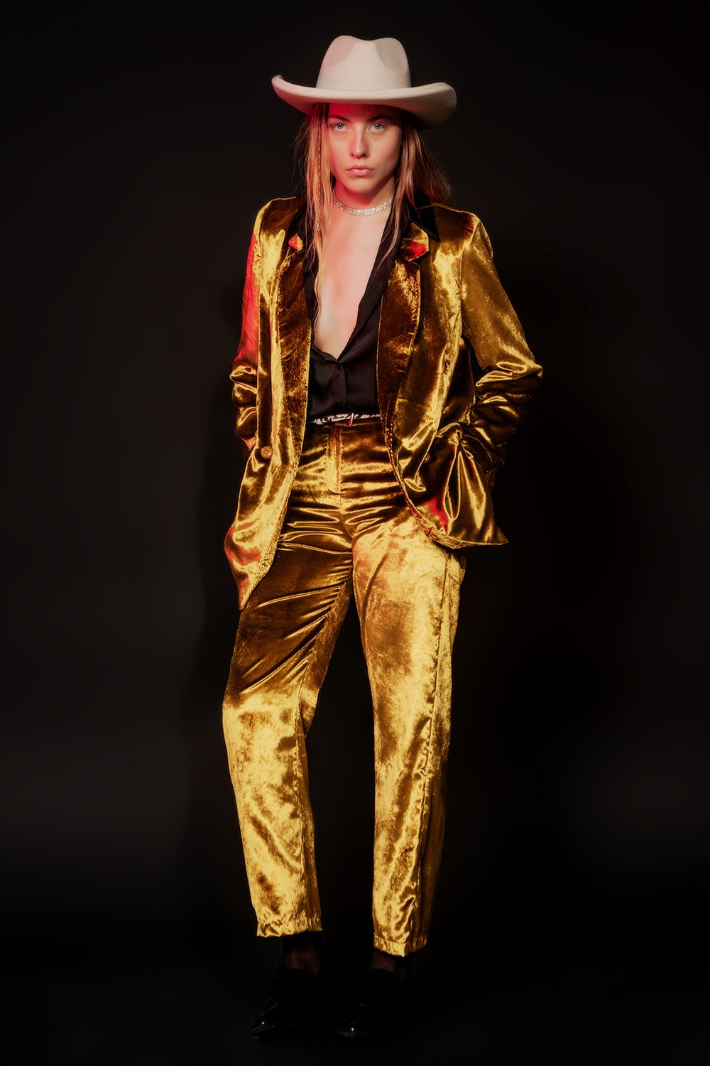 Modelo posando con traje completo de terciopelo brillante color lima dorado, camisa negra y sombrero.