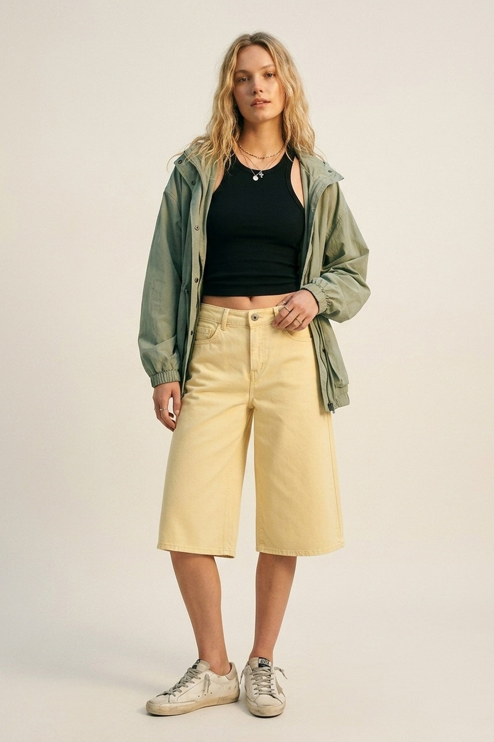 Bermudas vaqueras tipo culotte en color amarillo pastel de tiro alto, combinadas con top cropped negro y zapatillas deportivas envejecidas.