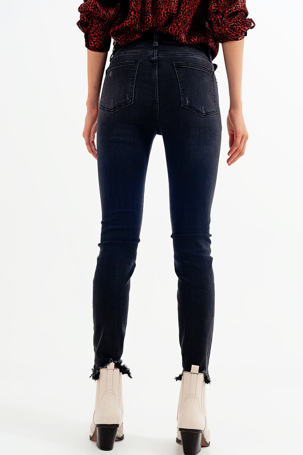 Mujer vistiendo vaqueros pitillo de talle alto en negro desgastado con bajo deshilachado y botines western beige