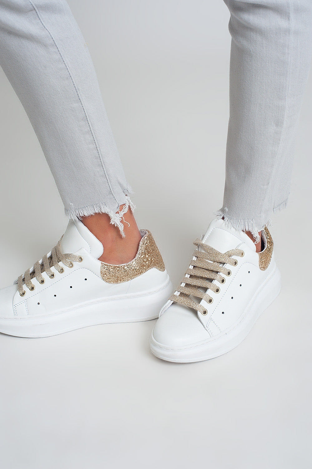 Detalle del bajo deshilachado con sneakers doradas