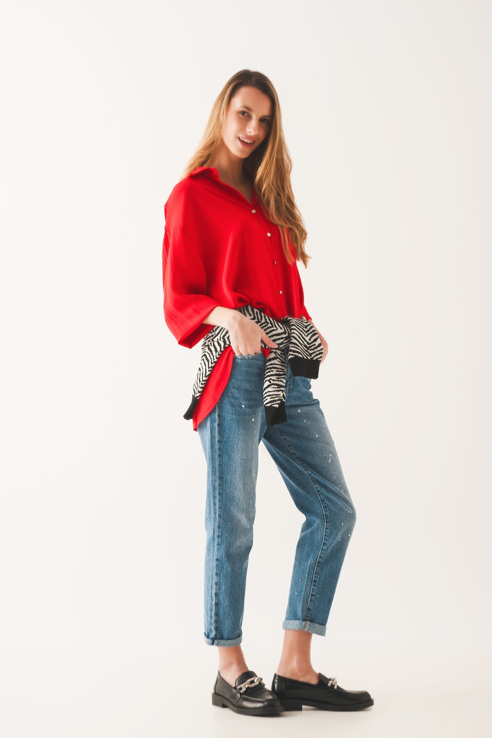 Mujer vistiendo vaqueros corte mom fit con detalles de salpicaduras de pintura blanca y camisa roja.