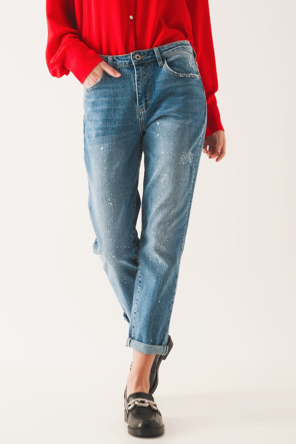 Mujer vistiendo vaqueros corte mom fit con detalles de salpicaduras de pintura blanca y camisa roja.