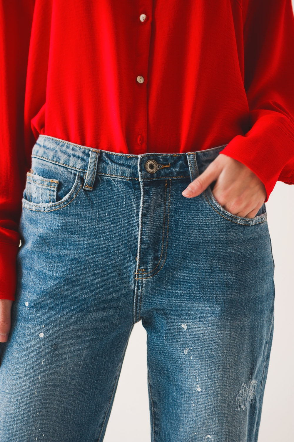 Mujer vistiendo vaqueros corte mom fit con detalles de salpicaduras de pintura blanca y camisa roja.