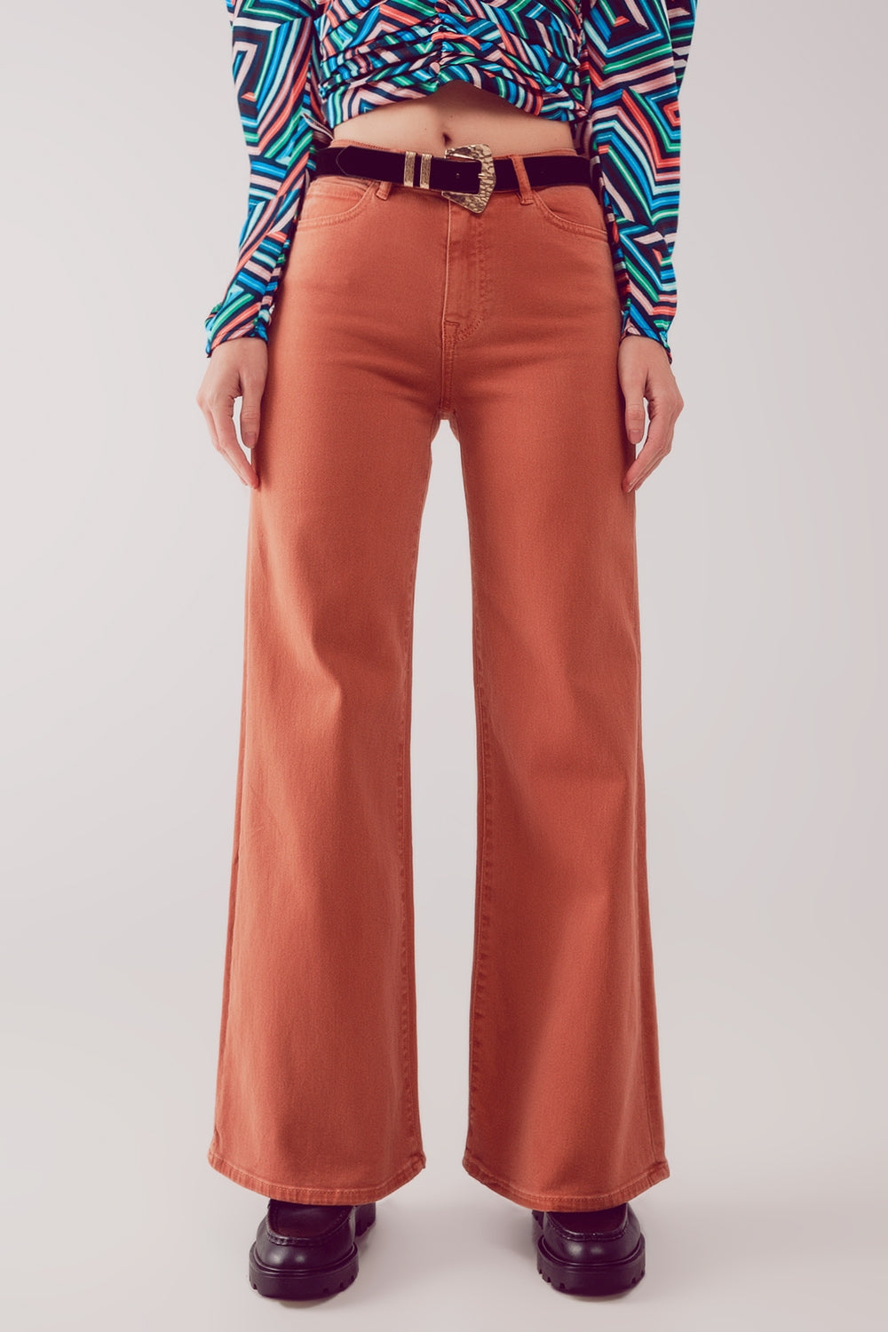 Modelo con pantalón acampanado de talle alto en color naranja teja y top estampado