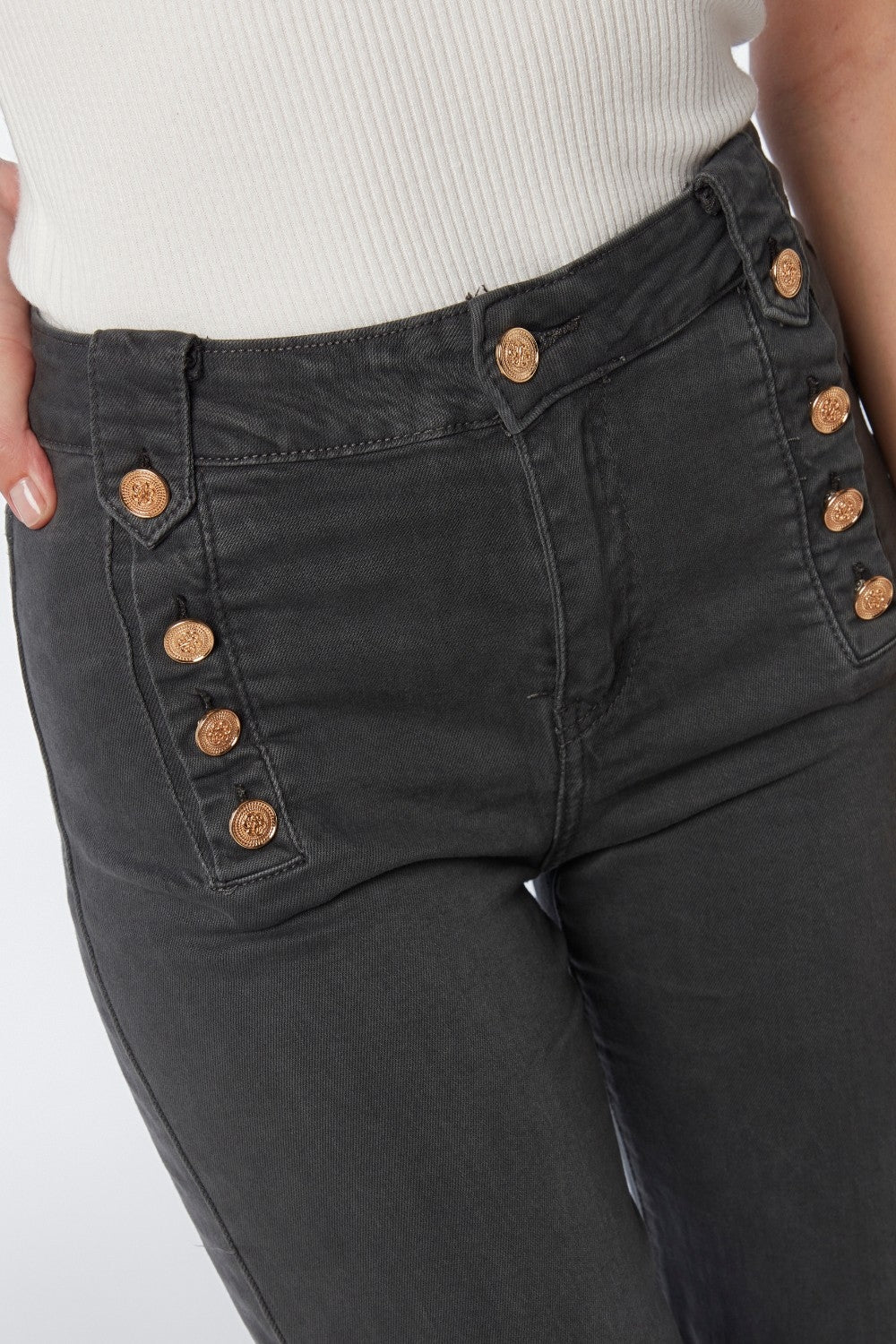 Primer plano de la doble botonadura dorada de un pantalón de talle alto estilo marinero.