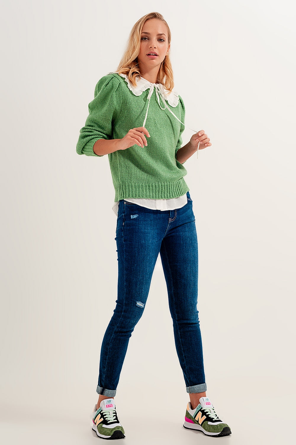 Look completo de vaquero pitillo azul, jersey de punto verde y zapatillas de deporte.