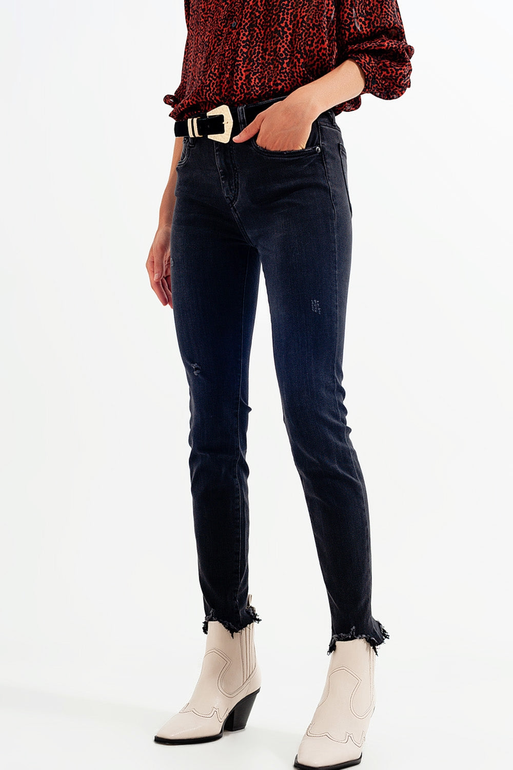 Mujer vistiendo vaqueros pitillo de talle alto en negro desgastado con bajo deshilachado y botines western beige