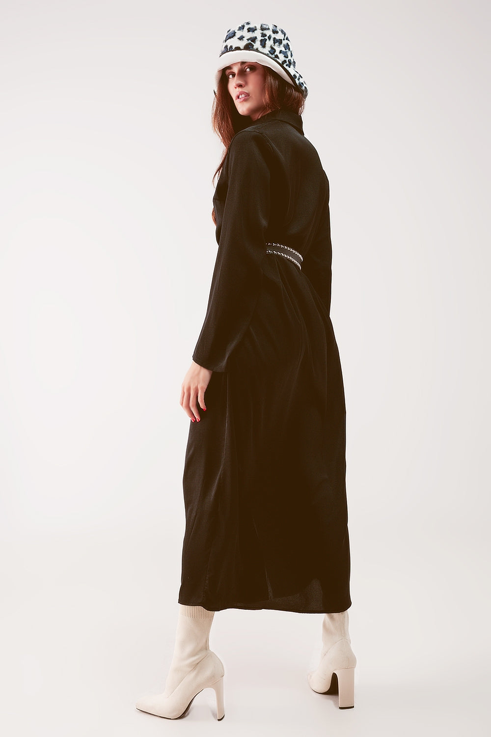 Vista de perfil de un vestido camisero largo de satén negro, mostrando su caída fluida.