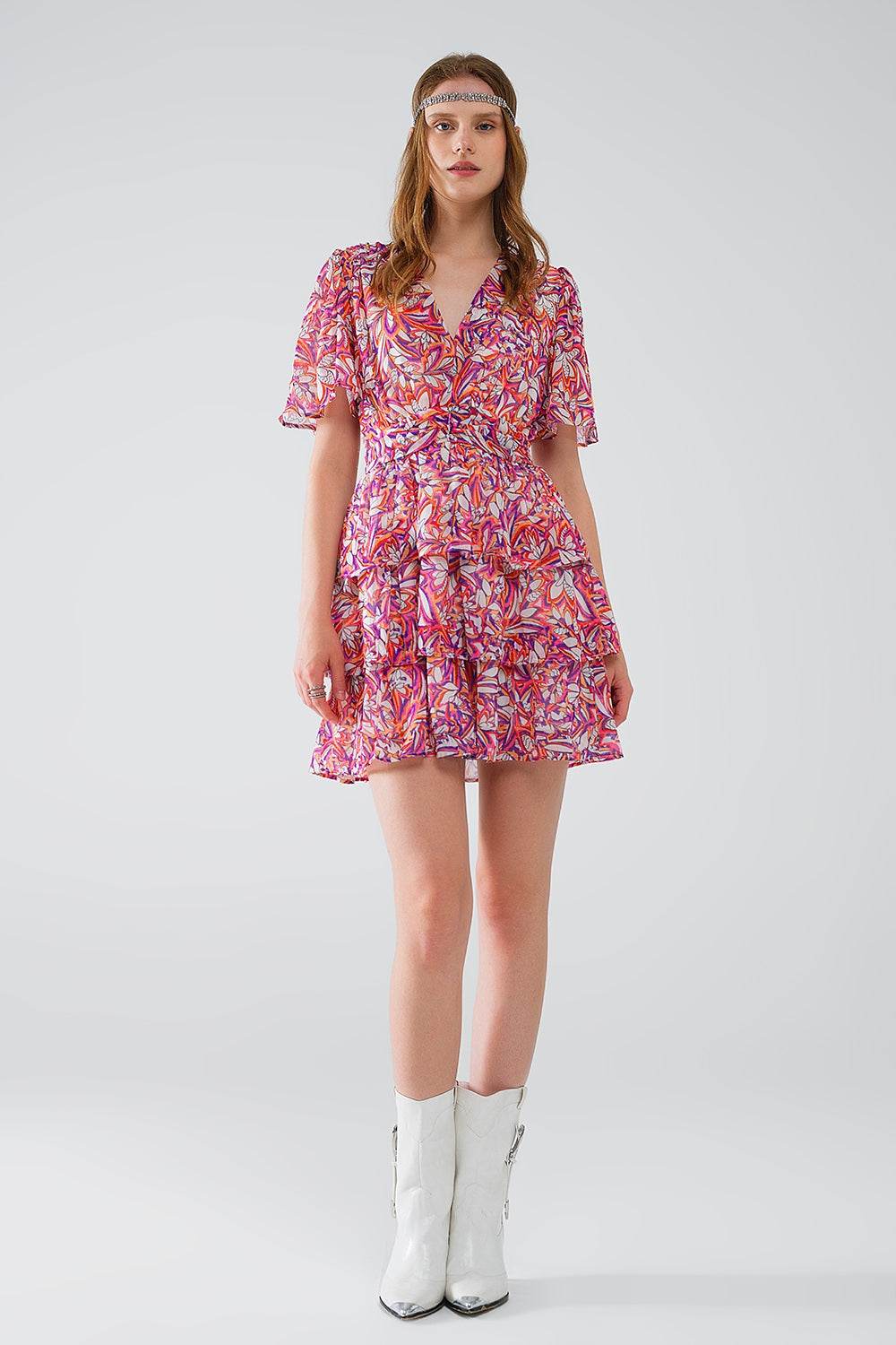 Mujer vistiendo vestido corto de gasa con estampado floral vibrante, volantes y botines blancos.
