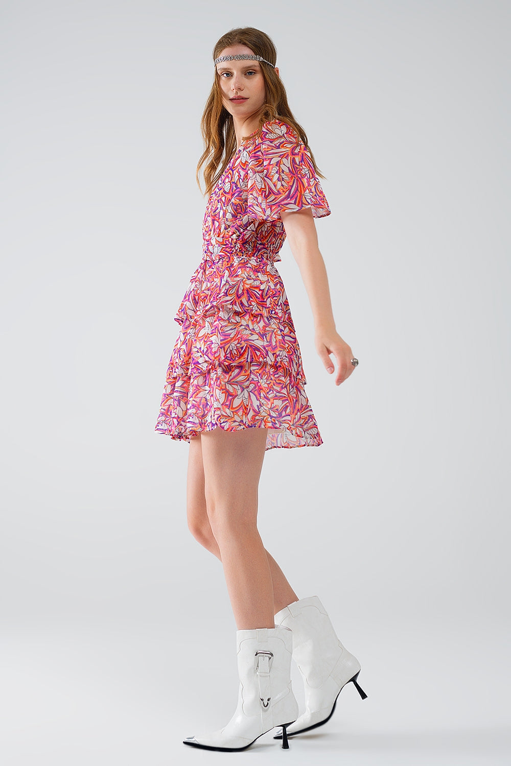 Mujer vistiendo vestido corto de gasa con estampado floral vibrante, volantes y botines blancos.