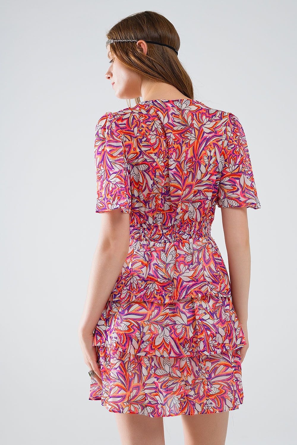 Mujer vistiendo vestido corto de gasa con estampado floral vibrante, volantes y botines blancos.