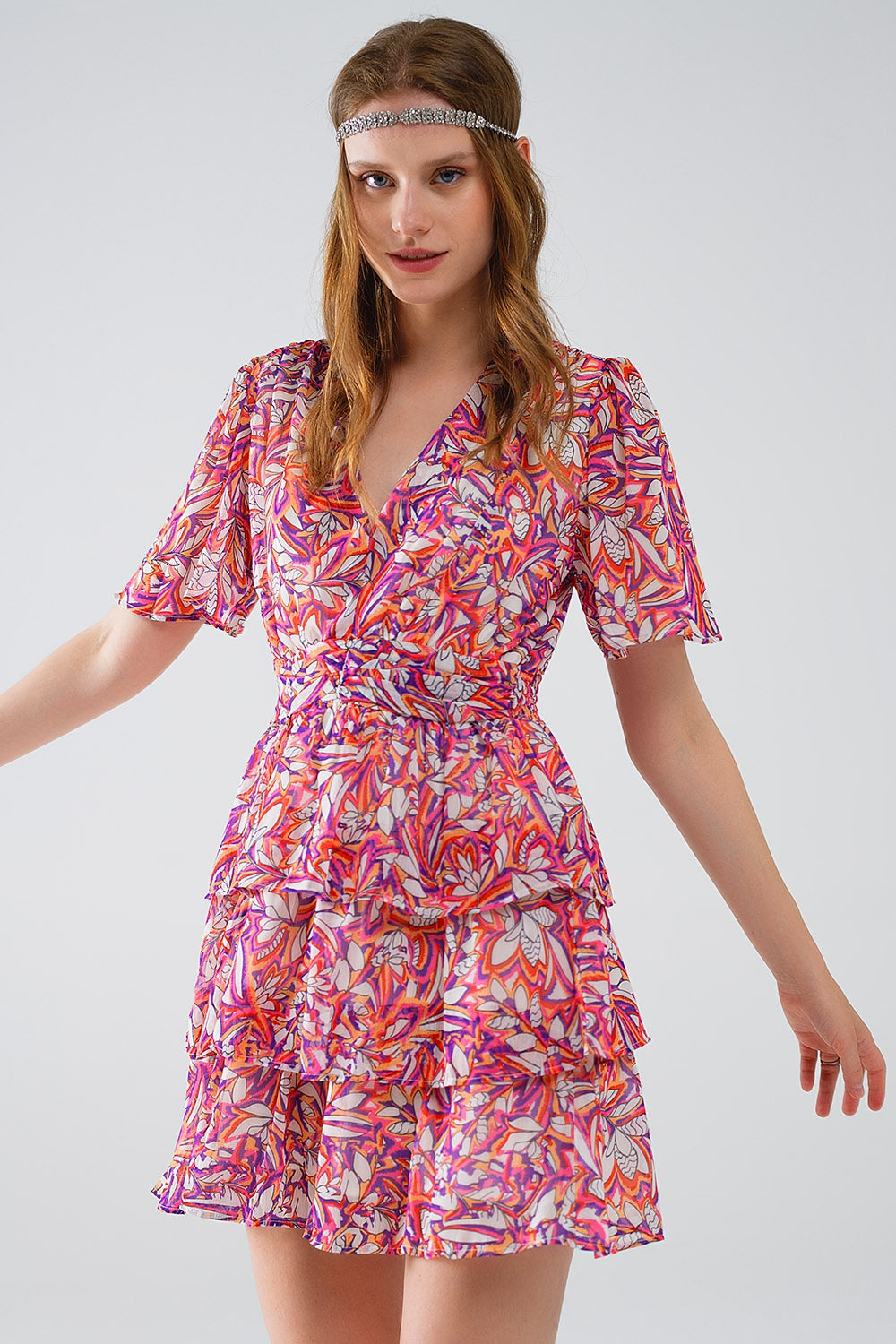 Mujer vistiendo vestido corto de gasa con estampado floral vibrante, volantes y botines blancos.