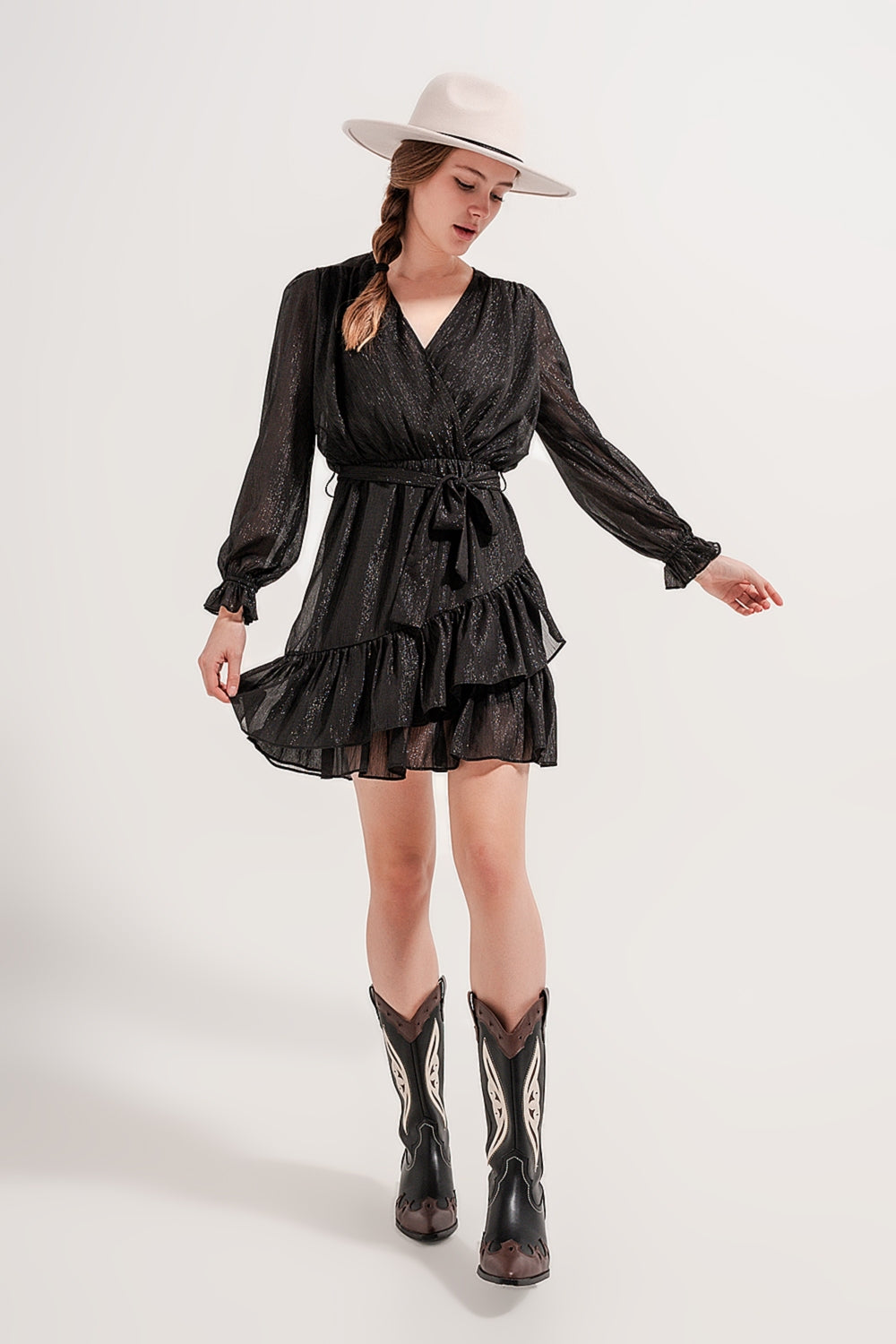 Modelo con mini vestido negro de fiesta con volantes, brillo de lúrex y botas cowboy.