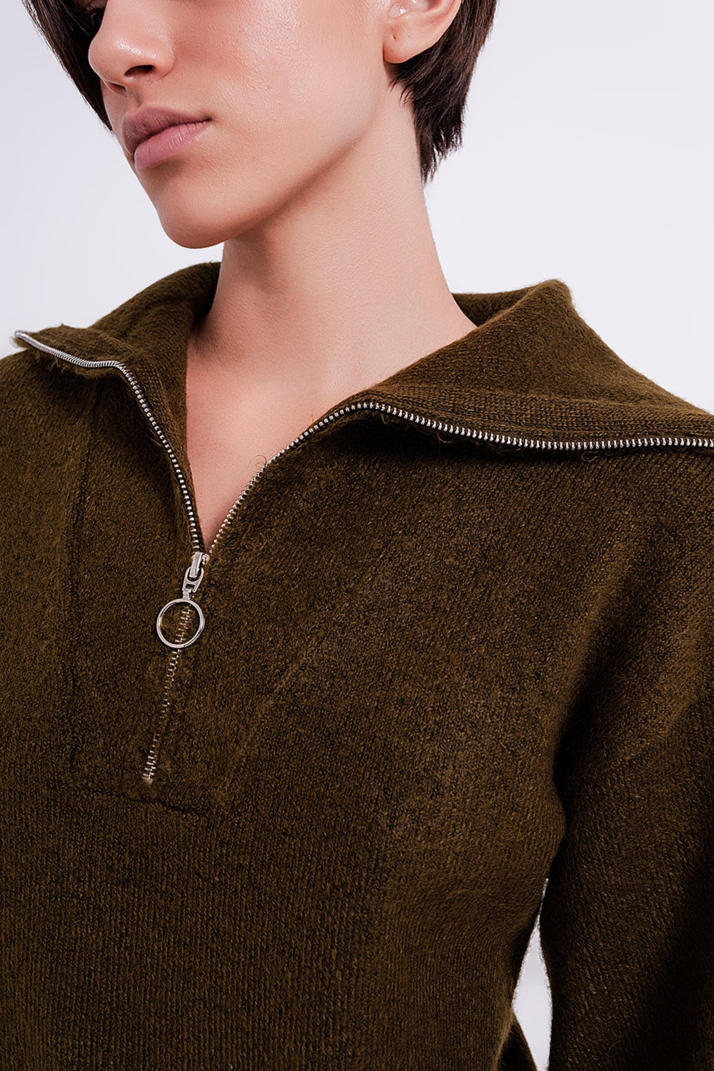 Primer plano del detalle de la cremallera metálica en el cuello alto de un vestido de punto verde.