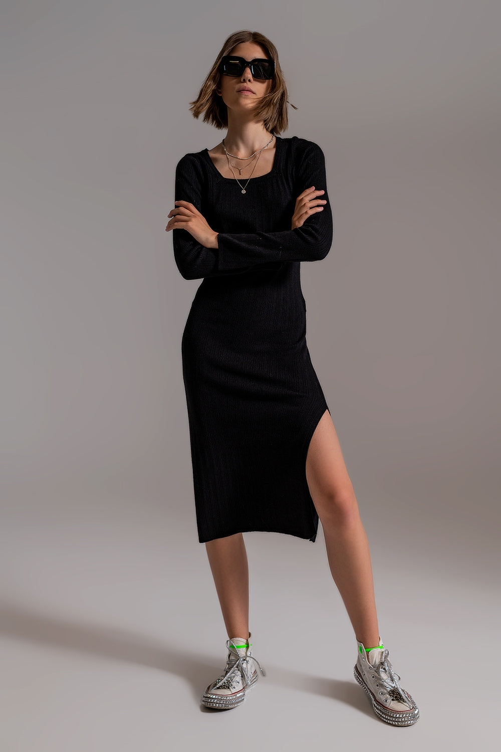 Modelo con vestido midi de punto ajustado en color negro, de manga larga y con escote cuadrado.