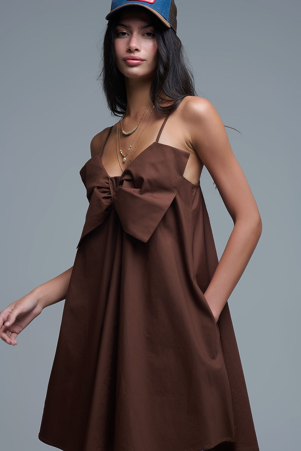 Primer plano del escote con lazo XXL del vestido marrón y collares dorados.