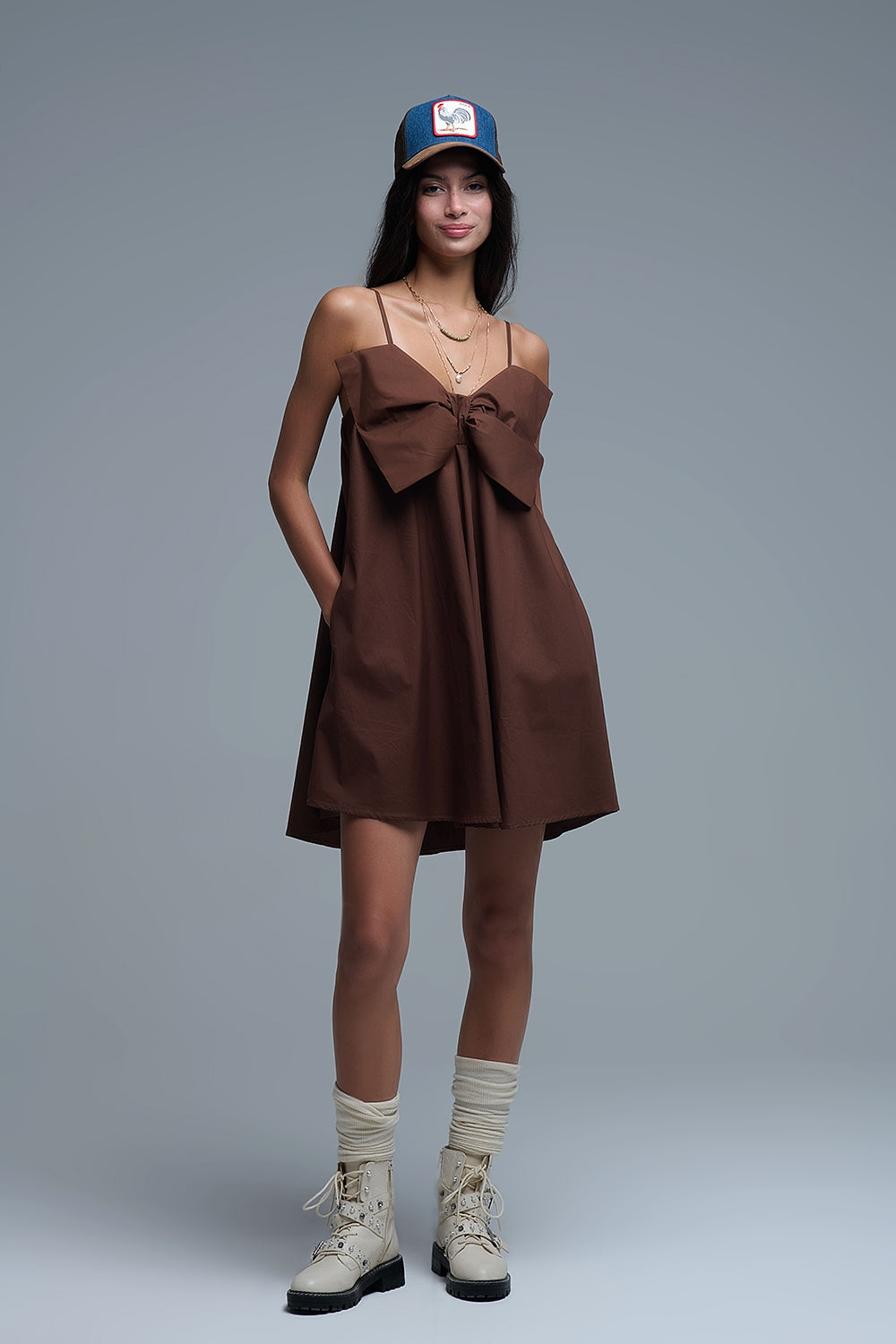 Mujer con vestido corto marrón, botas altas y gorra, estilo casual con actitud.