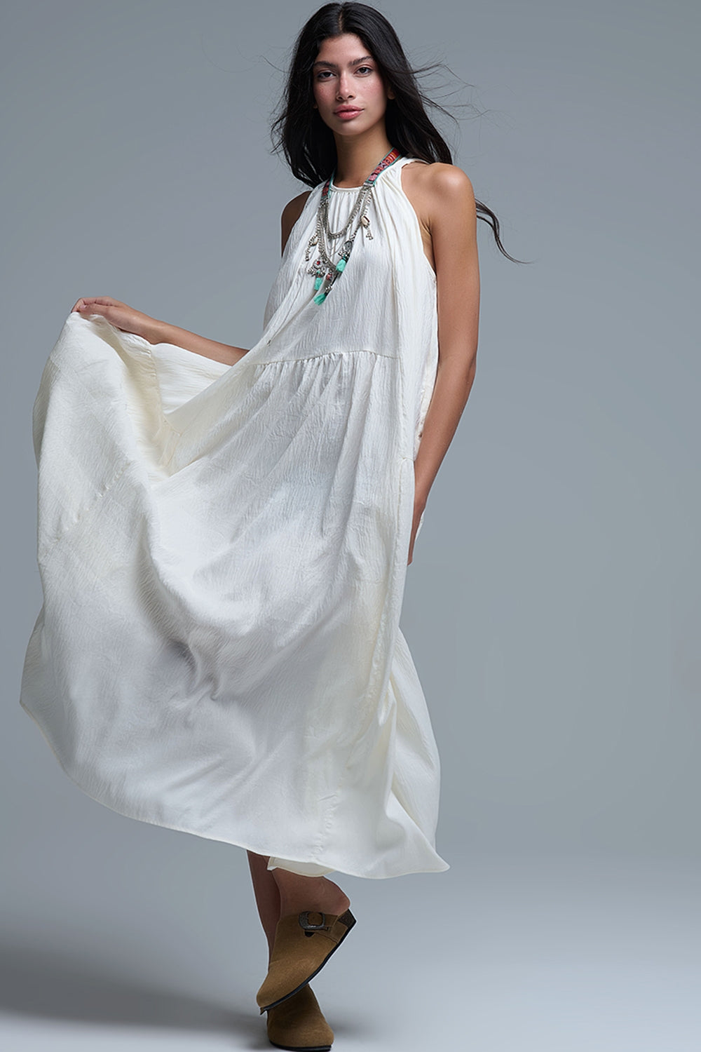 Vestido largo de color blanco roto con cuello halter y silueta maxi muy holgada, tejido texturizado con bolsillos laterales ocultos y collar étnico.