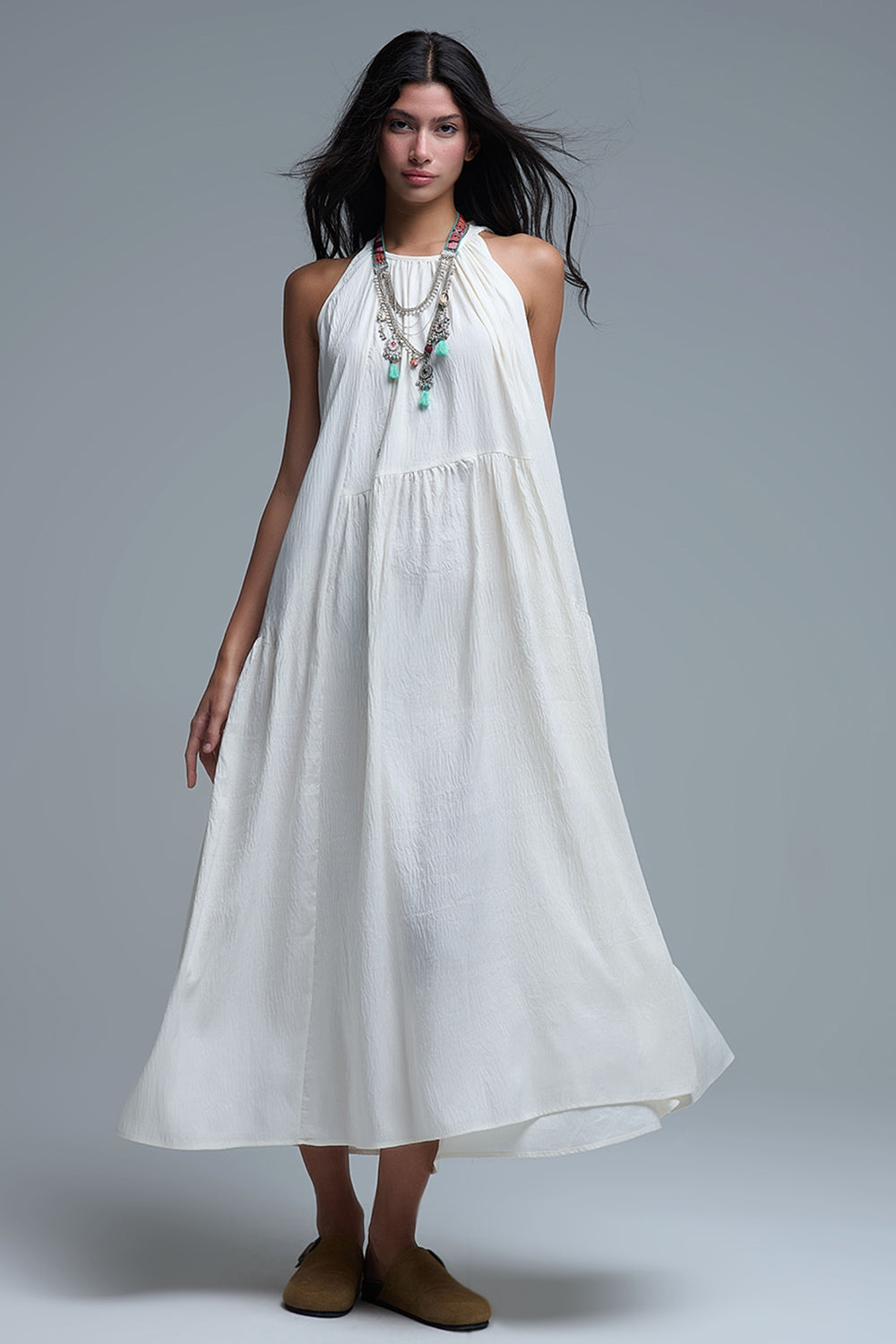 Vestido largo de color blanco roto con cuello halter y silueta maxi muy holgada, tejido texturizado con bolsillos laterales ocultos y collar étnico.