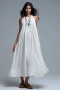 Vestido largo de color blanco roto con cuello halter y silueta maxi muy holgada, tejido texturizado con bolsillos laterales ocultos y collar étnico.