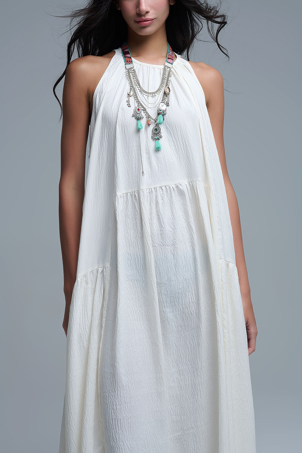 Vestido largo de color blanco roto con cuello halter y silueta maxi muy holgada, tejido texturizado con bolsillos laterales ocultos y collar étnico.