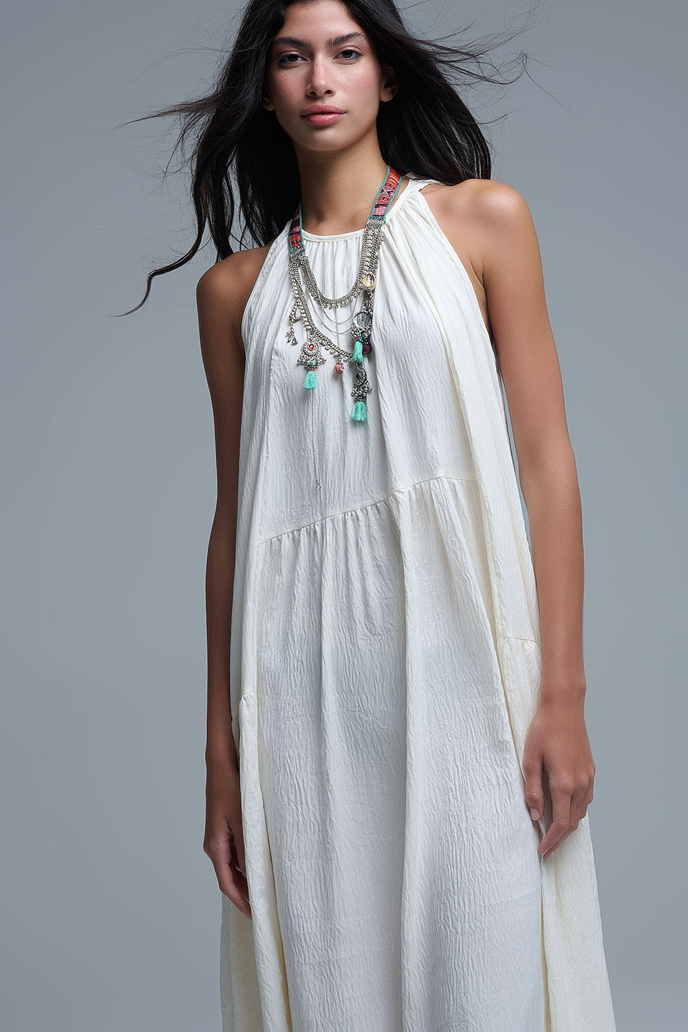 Vestido largo de color blanco roto con cuello halter y silueta maxi muy holgada, tejido texturizado con bolsillos laterales ocultos y collar étnico.