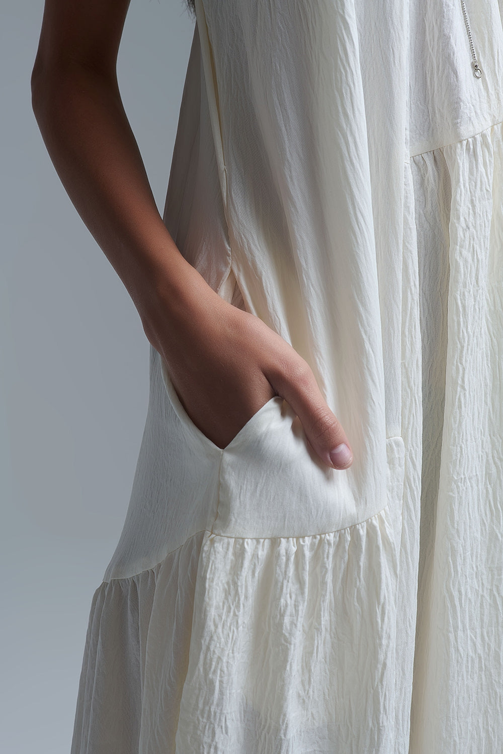 Vestido largo de color blanco roto con cuello halter y silueta maxi muy holgada, tejido texturizado con bolsillos laterales ocultos y collar étnico.