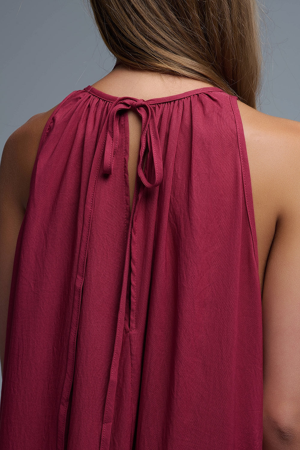 Vista trasera de vestido maxi burdeos con escote halter, espalda descubierta profunda y detalle de lazo ajustable en el cuello.