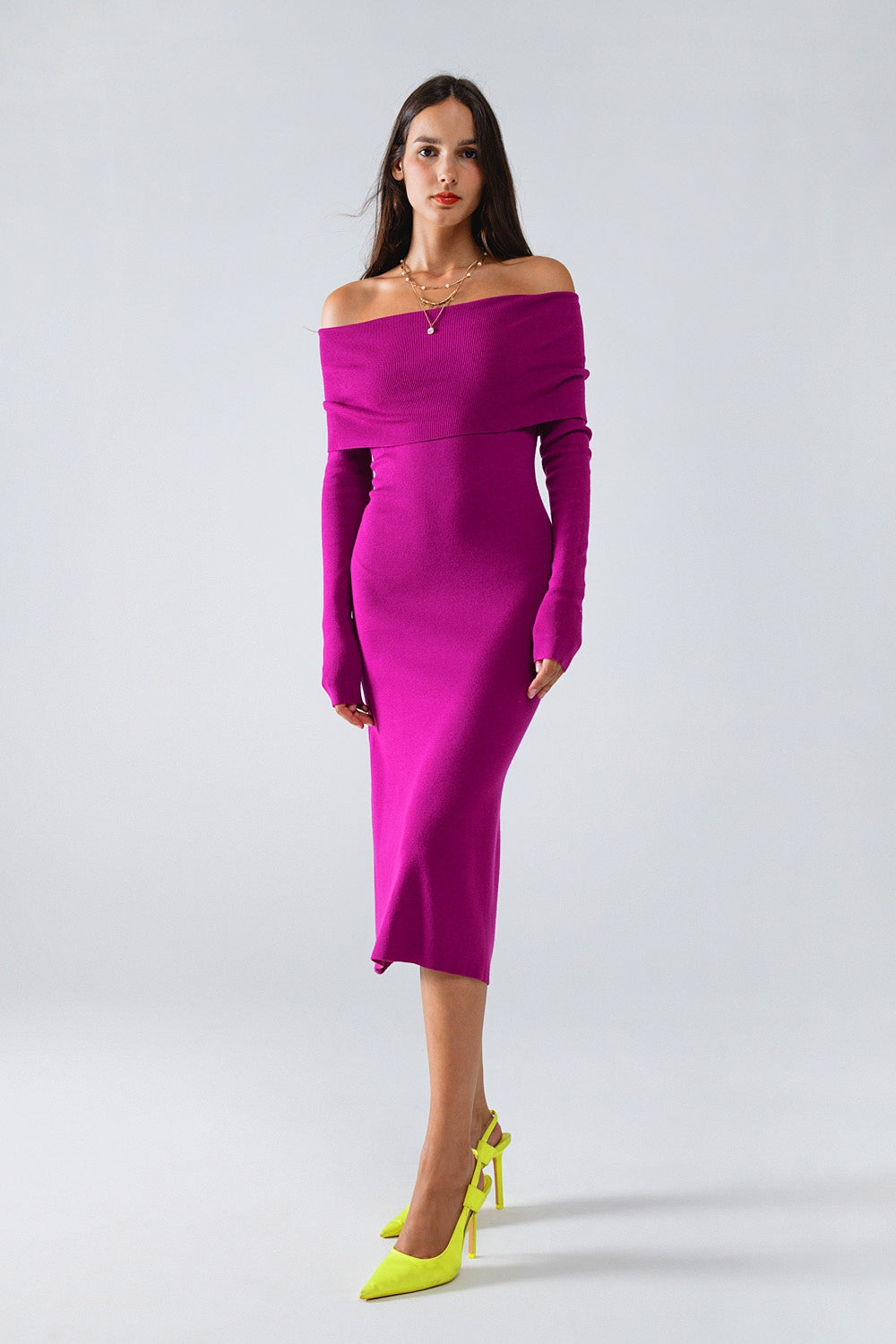 Modelo con vestido midi de punto ajustado en color magenta, con escote Bardot que deja los hombros al descubierto.