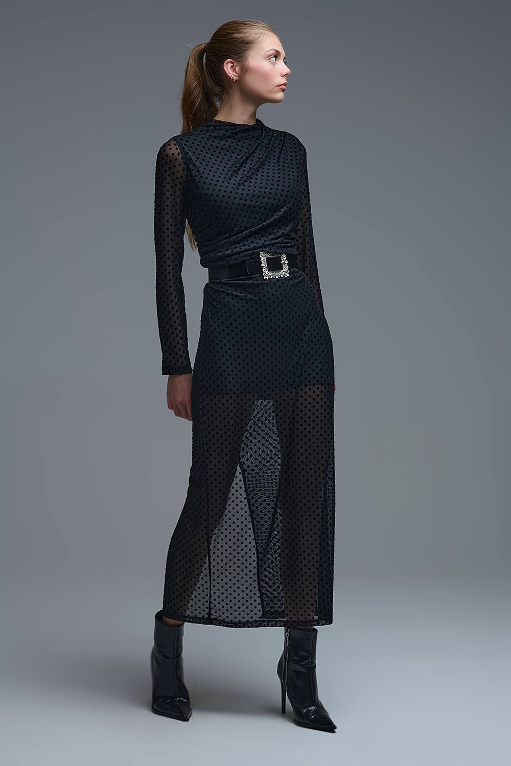 Modelo con vestido midi negro de gasa con lunares transparentes, manga larga y abertura en la pierna, combinado con cinturón de pedrería.