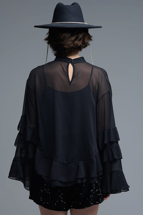 Vista trasera de una blusa negra transparente con diseño de capa y volantes en el bajo.