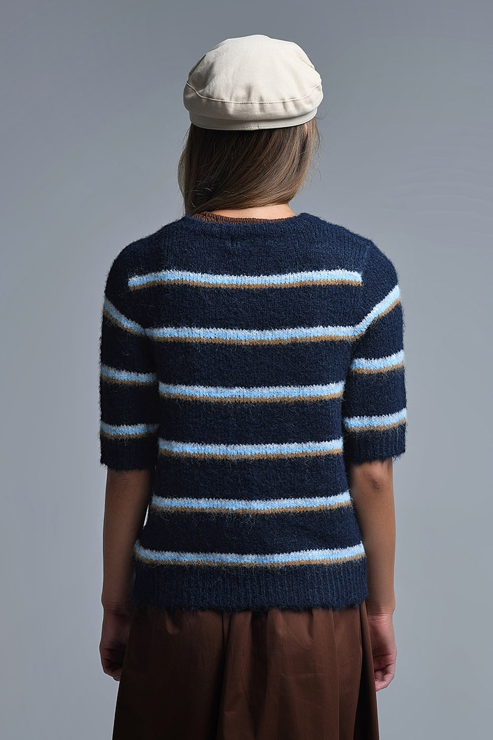 Vista trasera de una mujer con jersey de manga corta a rayas azul marino y gorra beige.