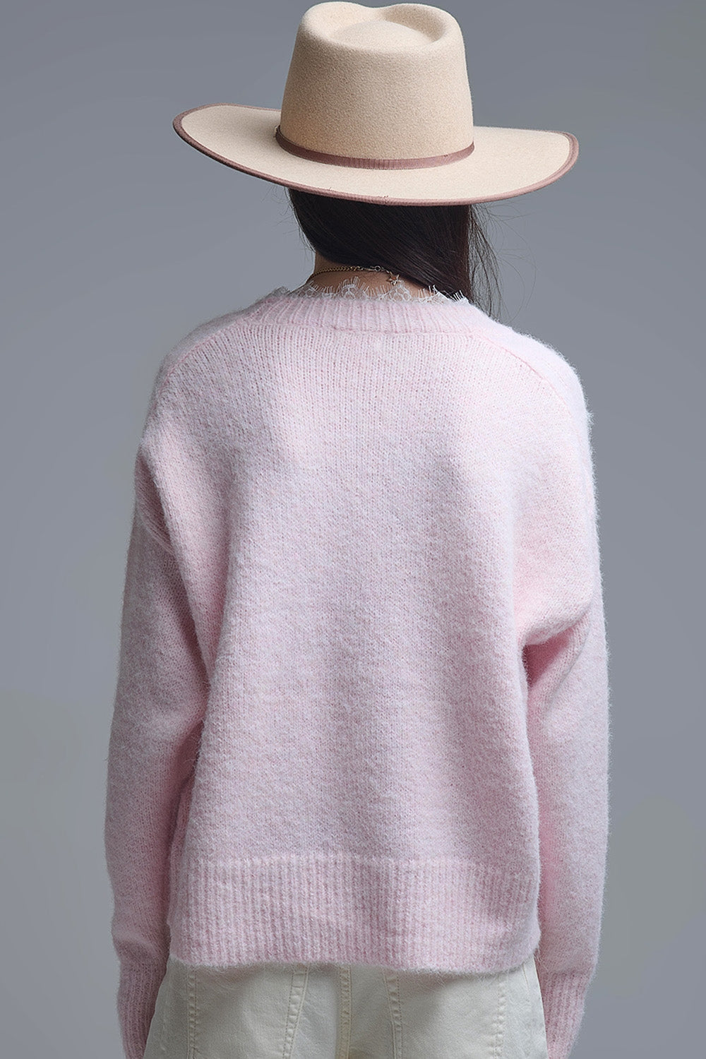 Vista trasera de una mujer con sombrero y jersey rosa de punto suave oversize.