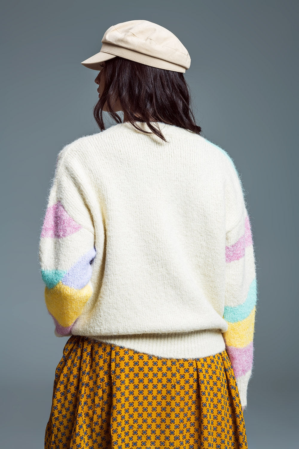 Parte trasera de un jersey de punto grueso beige con franjas de colores pastel mostrando el corte amplio.