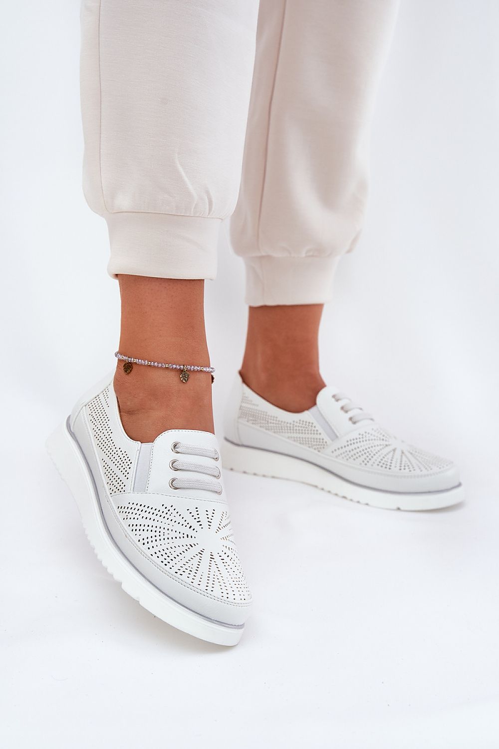 Mujer con joggers beige luciendo zapatillas blancas caladas con plataforma y elástico decorativo.