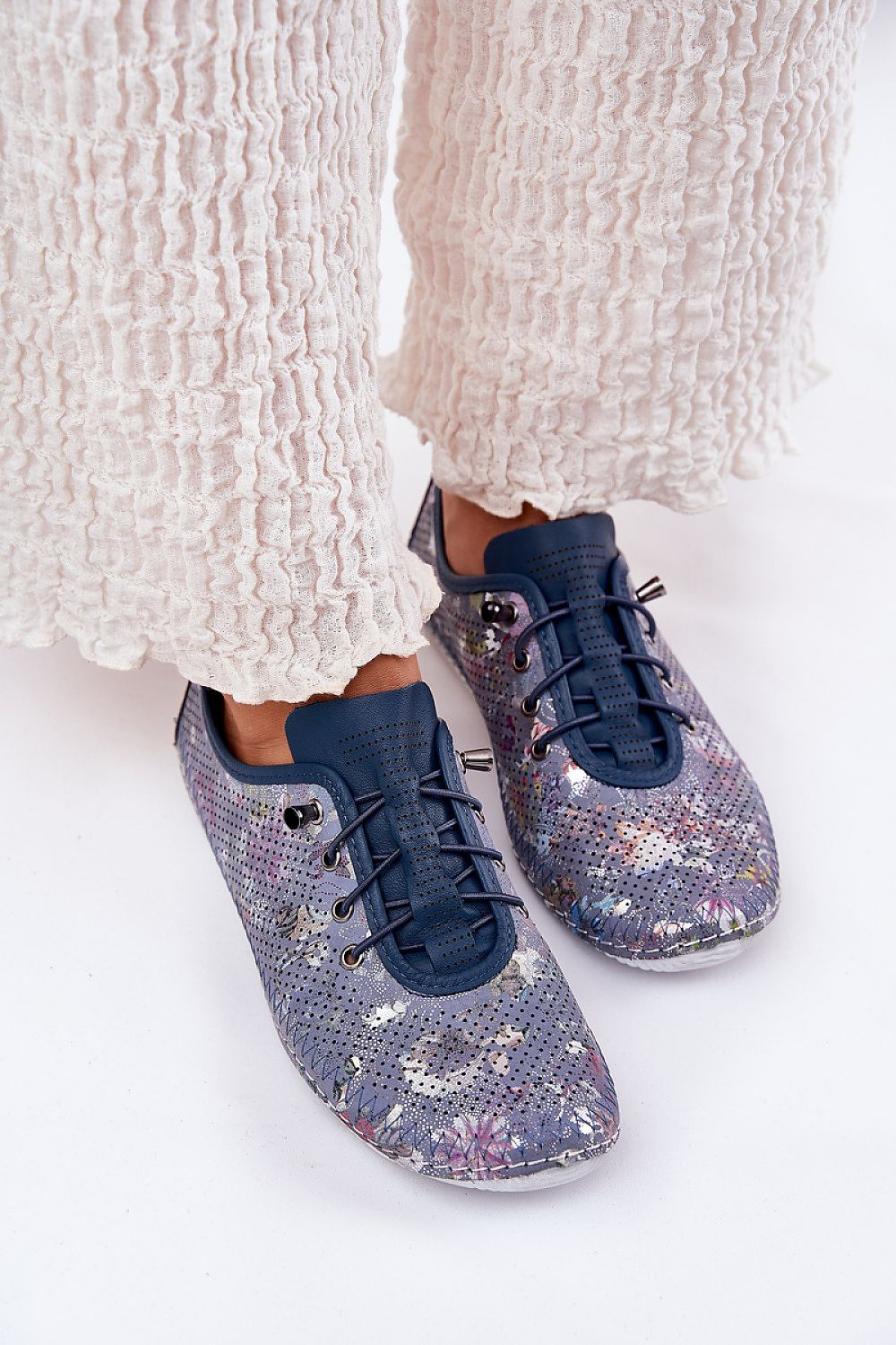 Zapatillas de piel en azul marino con estampado floral metalizado y elásticos, con pantalón blanco arrugado