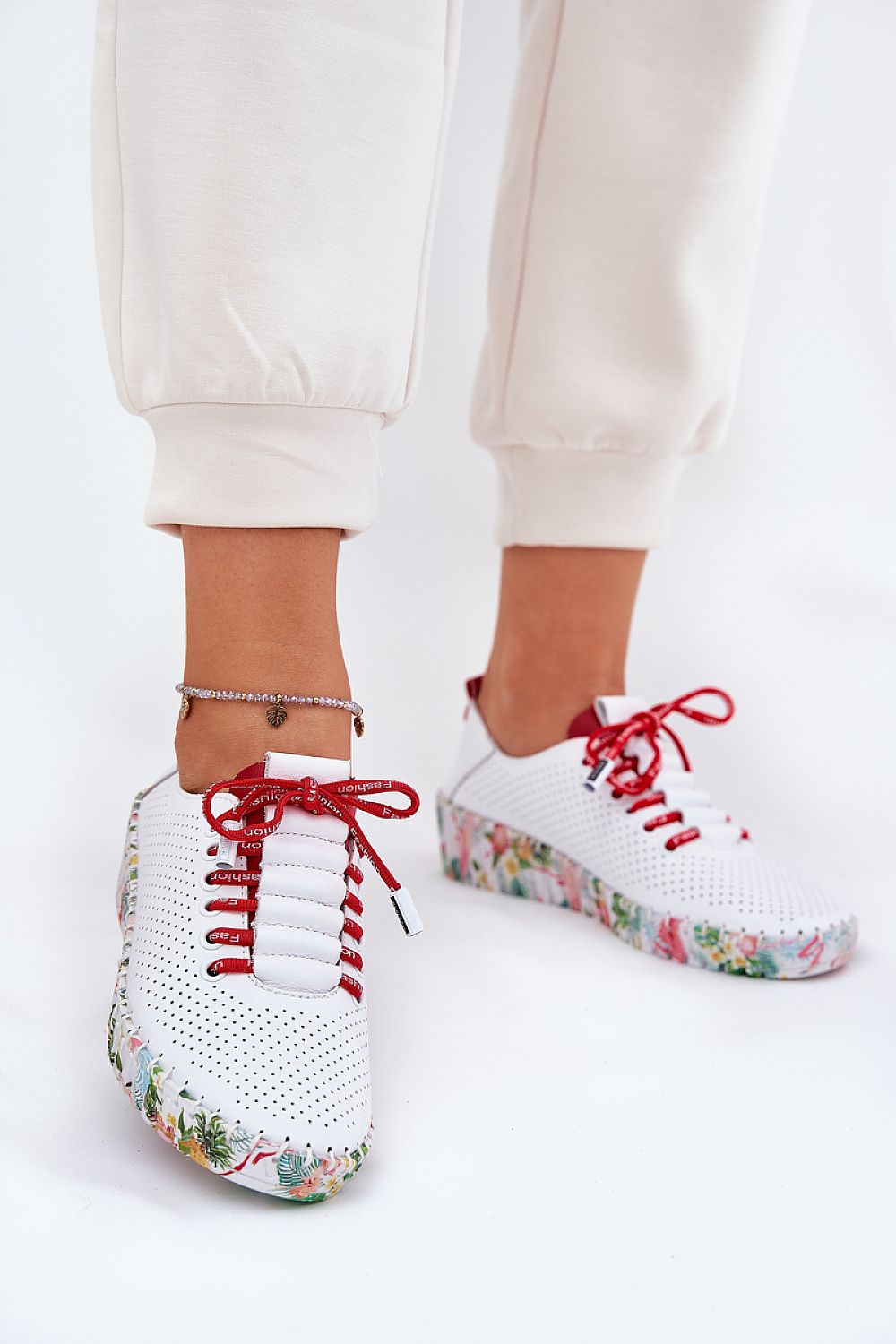 Zapatillas blancas con cordones rojos y suela floral, vista desde el frente